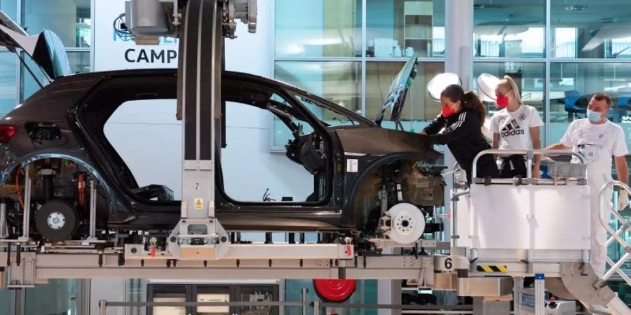 Die Nationalspielerinnen Sara Däbritz (l) und Merle Frohms (M) stehen in der Gläsernen Manufaktur von VW neben Montagemitarbeiter Gilbert Schulze an einem Volkswagen ID.3. Foto: Sebastian Kahnert/dpa-Zentralbild/dpa