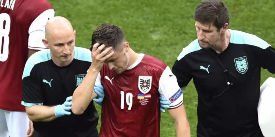 Der am Kopf verletzte Christoph Baumgartner (M) wird nach einer Verletzung von medizinischen Mitarbeitern vom Spielfeld geführt. Foto: Mihai Barbu/Pool AFP/AP/dpa