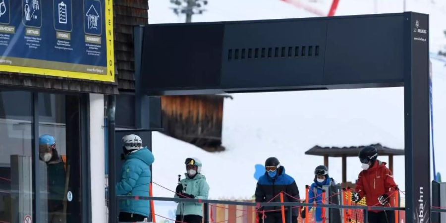 Wintersportler stehen in Tirol mit Mund-Nasen-Schutz an einem Skilift an. Foto: Helmut Fohringer/APA/dpa