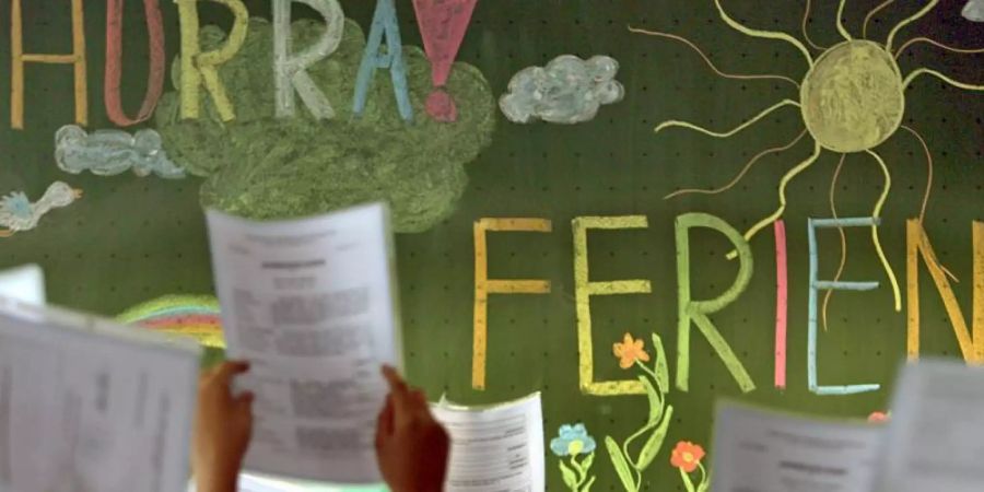 Kinder der vierten Klasse einer Grundschule in Kaufbeuren jubeln vor einer Tafel mit der Aufschrift «Hurra Ferien». Foto: Karl-Josef Hildenbrand/dpa