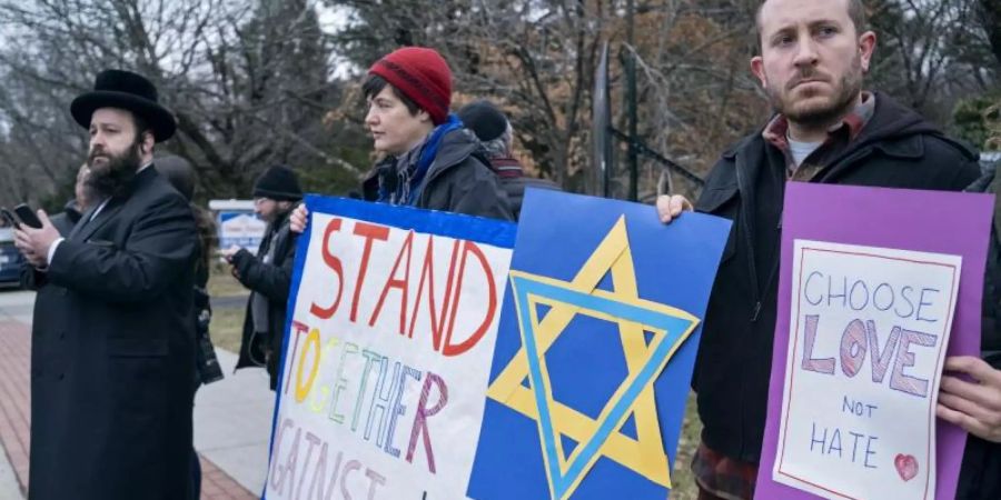 Nach dem Messerangriff am 28.12.2019 auf eine jüdische Chanukka-Feier mit mindestens fünf Verletzten nahe der Metropole New York stehen Menschen mit Schildern in der Nähe des Tatorts. Foto: Craig Ruttle/AP/dpa