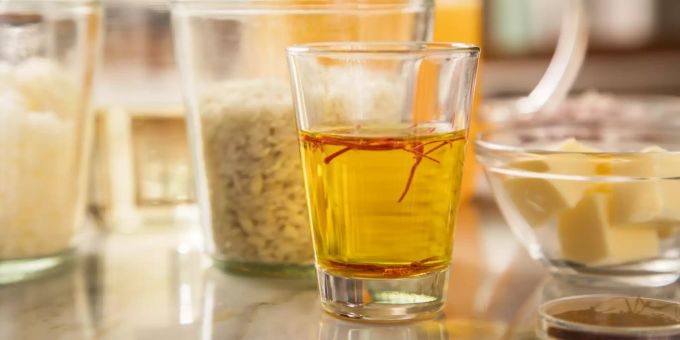 Bevor Safranfäden am Ende der Garzeit zum Beispiel einem Risotto hinzugefügt werden, sollten sie 10 bis 20 Minuten lang in etwas warmenm Wasser ziehen. Glas Wasser Safranfäden Gläser Butter Körner