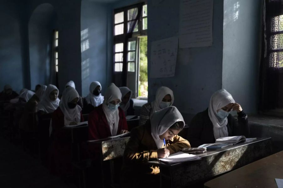 Afghanische Mädchen sitzen im Klassenzimmer über ihren Schulbüchern.