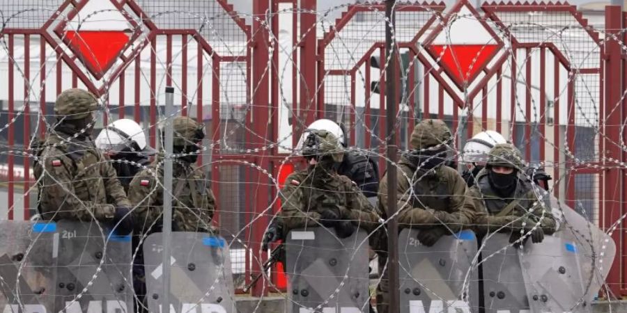 Polnische Sicherheitskräfte stehen hinter dem Grenzzaun am Grenzübergang Brusgi (Belarus) und Kuznica (Polen). Foto: Ulf Mauder/dpa