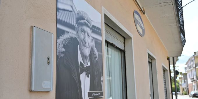 An der Fassade der Häuserin Perdasdefogu hängen Schwarz-Weiss-Fotos der Hundertjährigen aus dem Dorf mit deren Namen und Geburtsjahr. Auf diesem Bild ist Vittorio Lai zu sehen. Perdasdefogu Italien