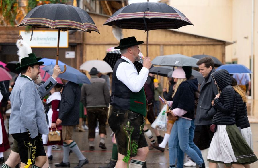 Wiesnbesucher gehen mit Regenschirmen über das Oktoberfestgelände.