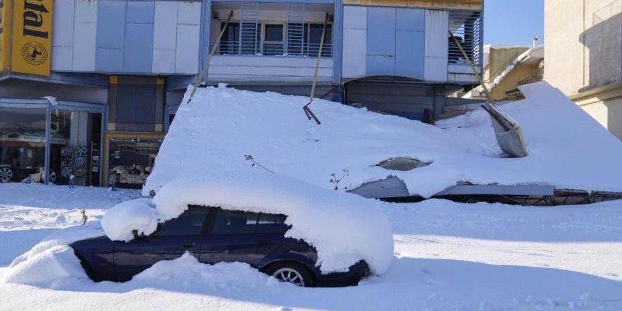 Ein schneebedecktes Auto steht vor einem beschädigten Gebäude. Über dem Grossraum Athen waren ungewöhnlich starke Schneefälle niedergegangen. Foto: Thanassis Stavrakis/AP/dpa