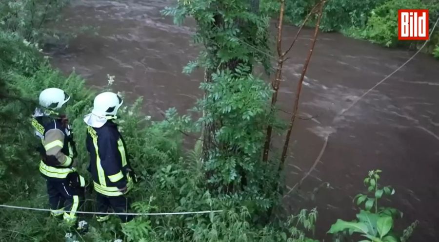 Die Feuerwehr spannt Seile über den Dorfbach, in der Hoffnung der Polizist kann sich daran festhalten, sollte er vorbeitreiben.