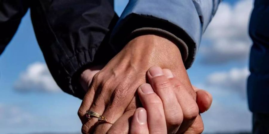 Eine Frau und ein Mann halten sich bei einem Strandspaziergang an den Händen. Foto: Axel Heimken/dpa