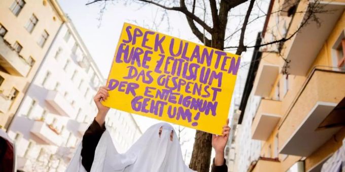 Eine Aktivistin im Gespensterkostüm hält ein Protestschild nahe dem Organisationsbüro des Volksbegehrens «Deutsche Wohnen & Co. enteignen» in die Kamera. Foto: Christoph Soeder/dpa Eine Aktivistin im Gespensterkostüm hält ein Protestschild nahe dem Organisationsbüro des Volksbegehrens «Deutsche Wohnen & Co. enteignen» in die Kamera. Foto: Christoph Soeder/dpa