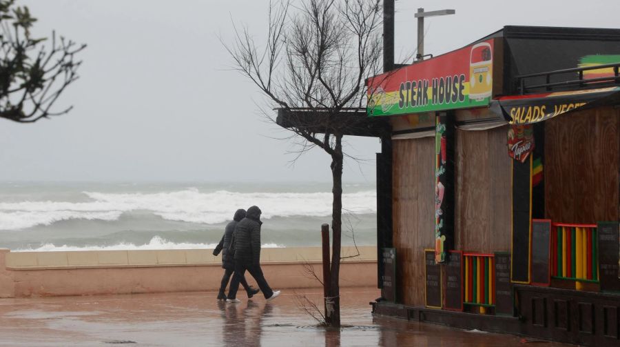 Ein Paar geht bei stürmischem Wetter an der Strandpromenade von Can Picafort auf Mallorca spazieren.