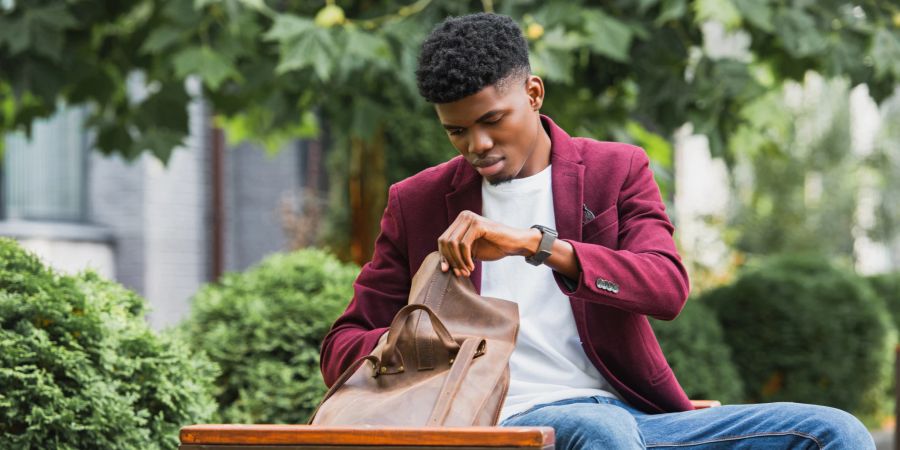 Mann mit weissem Shirt, Jeans und bordeauxfarbenem Blazer schaut in seine Tasche