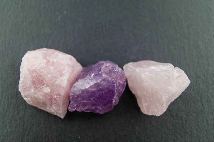 Während der Amethyst (m.) die Eigenschaften des Wassermanns unterstützen soll, gilt das Gleiche für den Rosenquarz (l. u. r.) in Verbindung mit dem Stier-Sternzeichen. Mineralsteine Amethyst und Rosenquarz