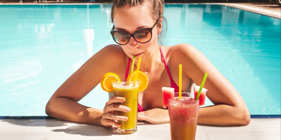 Frau trinkt Cocktail am Rande des Swimmingpools in einem All-inclusive-Hotel-Resort.