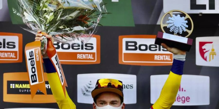 Der Slowene Primoz Roglic vom Team Jumbo jubelt mit Mund-Nasen-Schutz und Pokal bei der Siegerehrung auf dem Podium. Foto: Olivier Matthys/AP/dpa