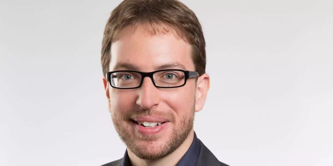 Mann mit brauen Haaren und Brille im Anzug