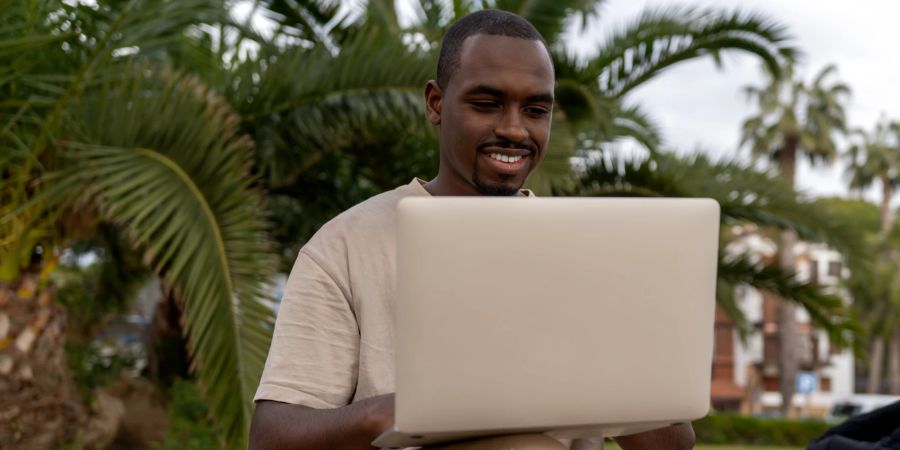 Mann mit Laptop, Palmen im Hintergrund