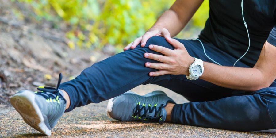 Sportler sitzt auf dem Boden, fässt sich ans Knie