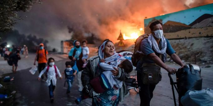 ARCHIV - 09.09.2020, Griechenland, Lesbos: Migranten fliehen vor einem erneuten Feuer mit ihren Habseligkeiten aus dem Flüchtlingslager Moria, nachdem zuvor bereits mehrere Feuer das Lager nahezu vollständig zerstört haben. Brand in Flüchtlingslager Moria
