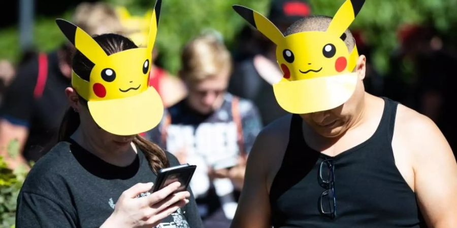 Zwei Teilnehmer mit Pokemon-Sonnenschutz spielen im Westfalenpark in Dortmund auf ihren Handys "Pokemon Go" (Archivbild vom 30.6.2018). Foto: Marcel Kusch/dpa