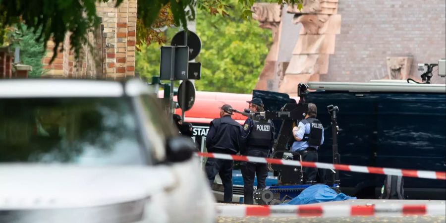 Polizisten sichern an der Mauer zur Synagoge die Umgebung, eine abgedeckte Leiche liegt auf der Strasse.