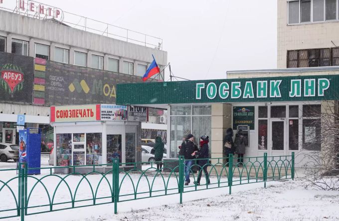 Bürger stehen vor einer Filiale der Gosbank (Staatsbank) der LNR mit einer Flagge der international nicht anerkannten Volksrepublik Luhansk (LNR). Luhansk