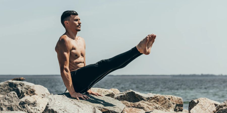 Mann in Yoga-Position auf einem Felsen.