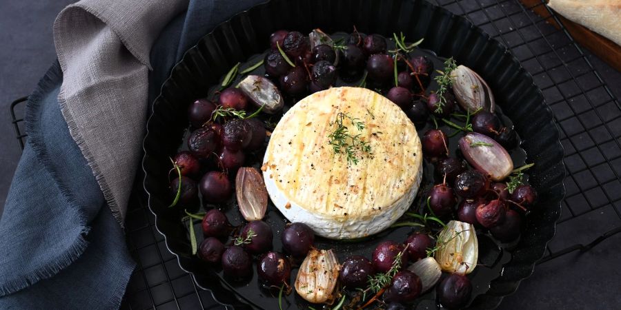 Der Camembert kommt in die Mitte, Schalotten und Tafeltrauben drumherum. Getoppt mit einem würzigen Dressing kommt das Blech in den Ofen.