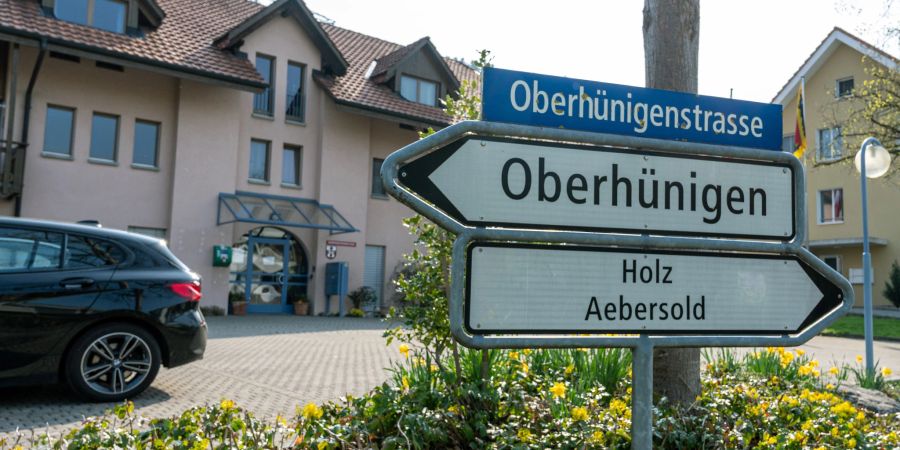 Ein Strassenwegweiser in Oberhünigen, Richtung Holz Äbersold an der Oberhünigenstrasse. Im Hintergrund die Gemeindeverwaltung von Niederhünigen an der Dorfstrasse 14.