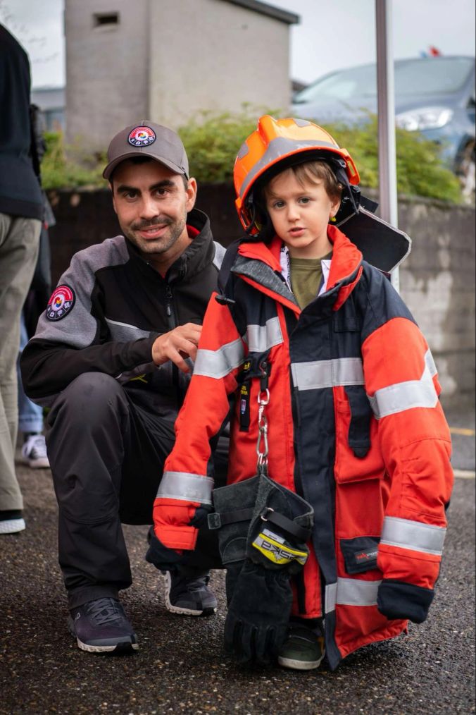 Feuerwehrmann Dominik Gubsler hilft Cursano beim Anprobieren einer Feuerwehr-Uniform.