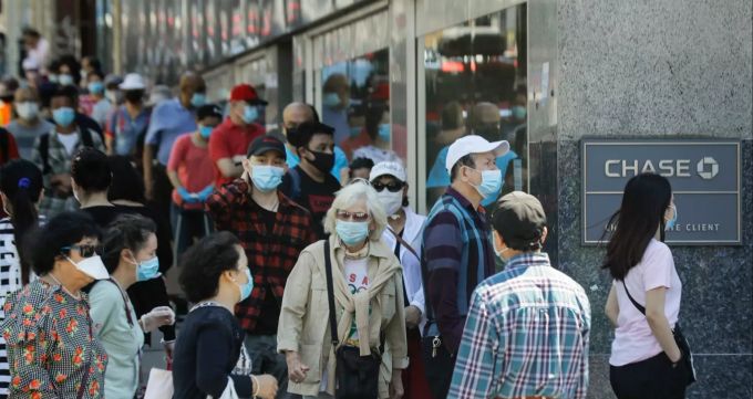 Menschen mit Masken warten im New Yorker Stadtbezirk Queens vor dem Eingang einer Bank. Coronavirus - USA