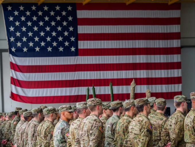 ARCHIV - 09.03.2017, Bayern, Illesheim: US-Soldaten stehen während einer militärischen Zeremonie in den Storck-Barracks vor einer Flagge der Vereinigten Staaten von Amerika. Die angeblichen Pläne von US-Präsident Trump, die Präsenz der amerikanischen Truppen in Deutschland deutlich zu reduzieren, sind in Berlin äusserst zurückhaltend aufgenommen worden. US-Truppen in Deutschland