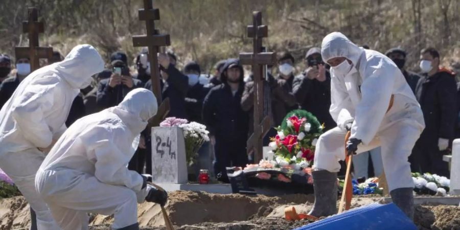 Totengräber in Schutzkleidung lassen auf einem Friedhof im russischen Kolpino den Sarg eines Covid-19-Opfers in ein Grab hinab. Foto: Dmitri Lovetsky/AP/dpa