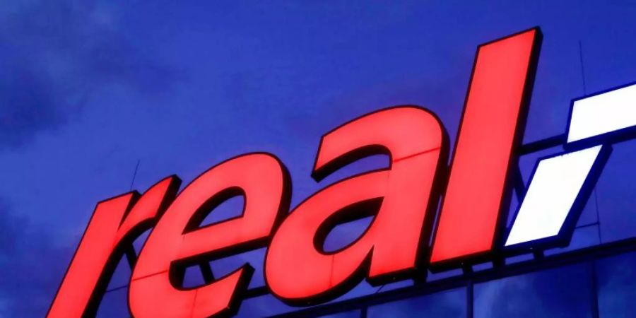 Das Real-Logo leuchtet am Morgen auf dem Dach eines Real Warenhauses in Köln. Foto: Oliver Berg/dpa