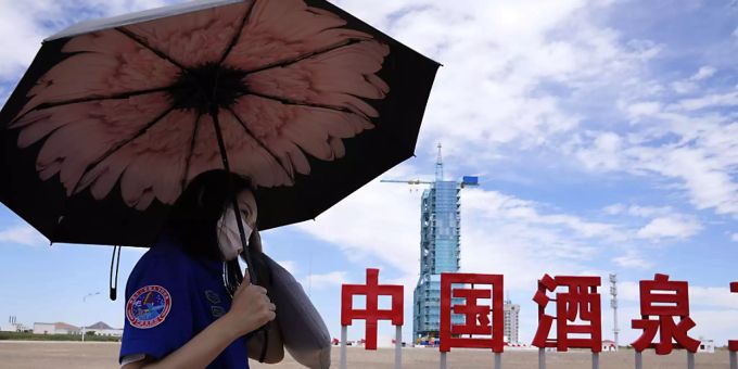 Ein Arbeiter hält einen Regenschirm in der Nähe des Raumschiffs Shenzhou-12, das auf der Startrampe mit den chinesischen Schriftzeichen «China Jiuquan Satellite Launch Center» steht. Foto: Ng Han Guan/AP/dpa Raumfahrt