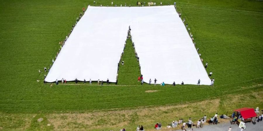 Menschen stehen auf einer Wiese und präsentiere eine überdemensional grosse Hose. Foto: Urs Flueeler/KEYSTONE/dpa
