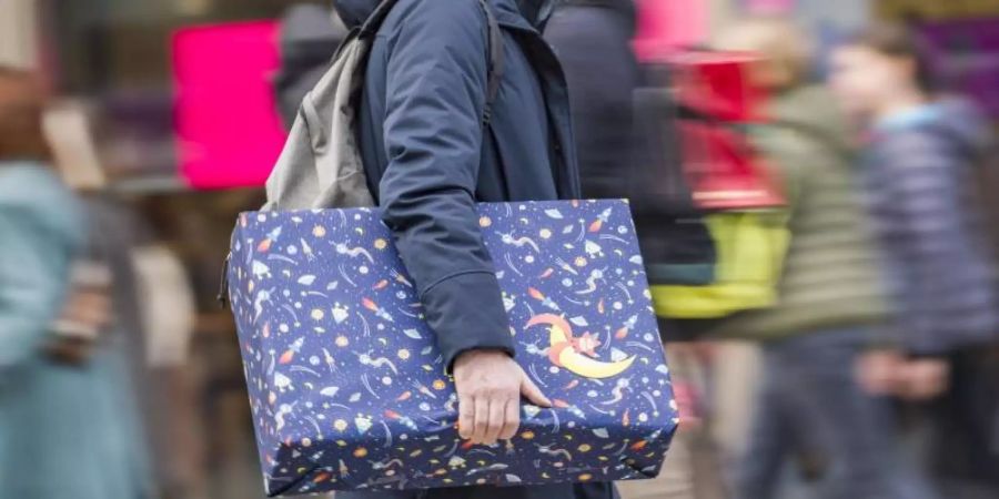 Ein Mann eilt mit einem verpackten Geschenk zwischen den anderen Passanten eine Einkaufsmeile entlang. Symbolbild). Foto: Frank Rumpenhorst/dpa