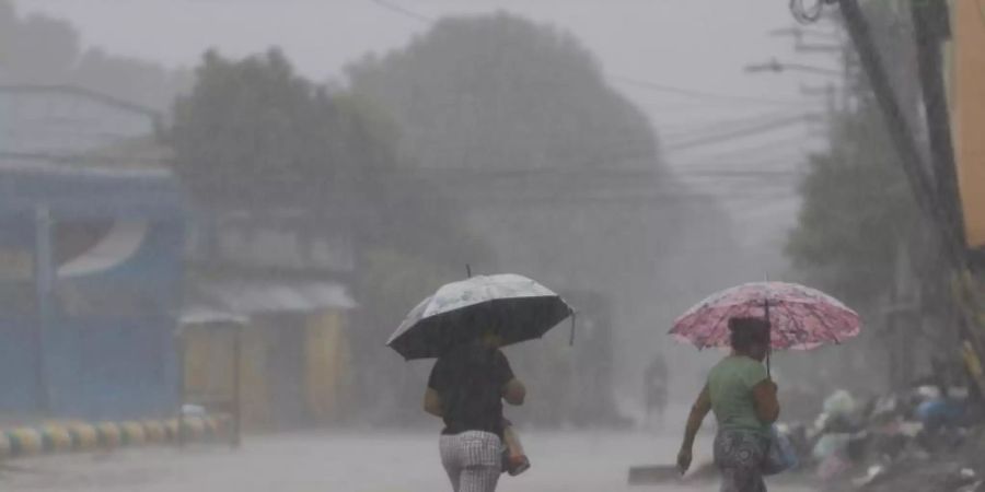 Zwei Frauen überqueren bei starkem Regen eine Strasse in La Lima in Honduras. Foto: Delmer Martinez/AP/dpa