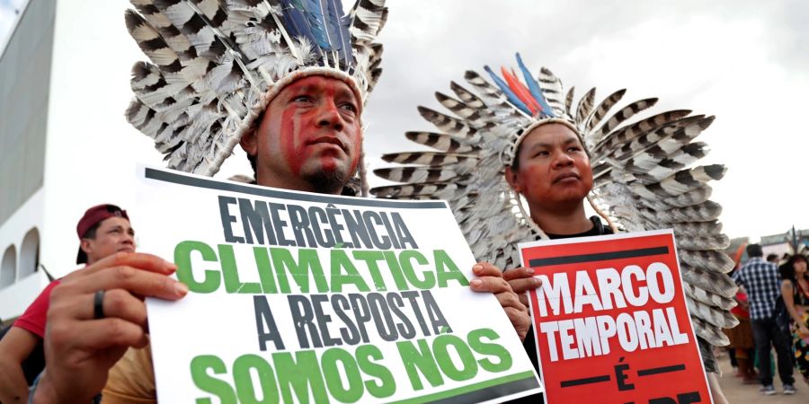 «Klima-Notstand - die Antwort sind wir» steht auf dem Plakat (r) eines indigenen Demonstranten, der in Brasilia gegen den Gesetzesentwurf zur Ausweisung von Schutzgebieten protestiert.
