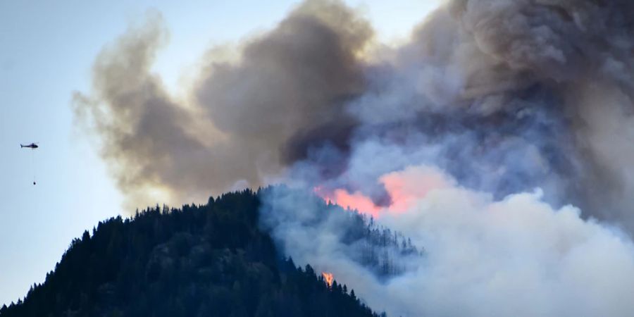 Ein Helikopter (links) nähert sich mit Löschwasser dem Brandherd oberhalb von Bitsch/Ried-Mörel im Oberwallis.