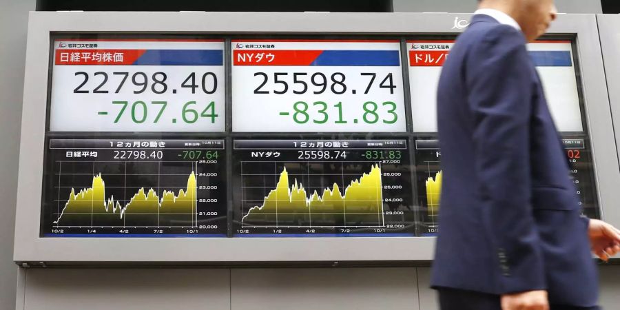 Ein Mann geht an einem Monitor vorbei, auf dem die Verluste an der Börse in Tokio (l) und an der Börse in New York angezeigt werden.