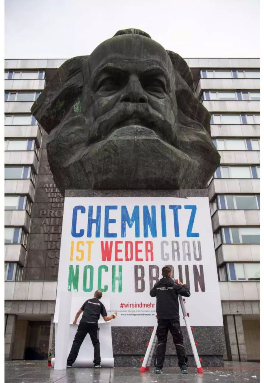 Zwei Männer befestigen am Chemnitzer Karl-Marx-Denkmal ein Plakat mit der Aufschrift «Chemnitz ist weder grau noch braun».