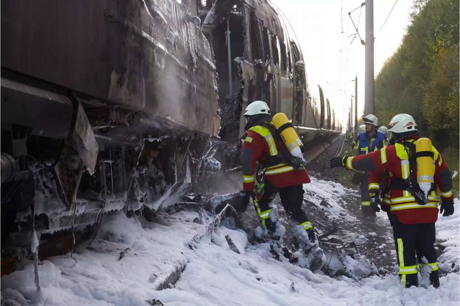 Feuerwehrleute sind nach dem Brand eines ICE auf der Schnellstrecke zwischen Köln und Frankfurt in der Nähe von Montabaur mit Nachlöscharbeiten beschäftigt. Auf dem Boden liegt Löschschaum.