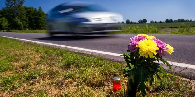 Blumen und ein Grablicht stehen an einer Unfallstelle.