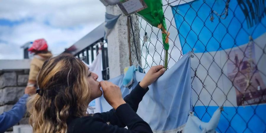 Eine Frau befestigt eine Blume an einem Zaun vor dem Marinestützpunkt von Mar del Plata.