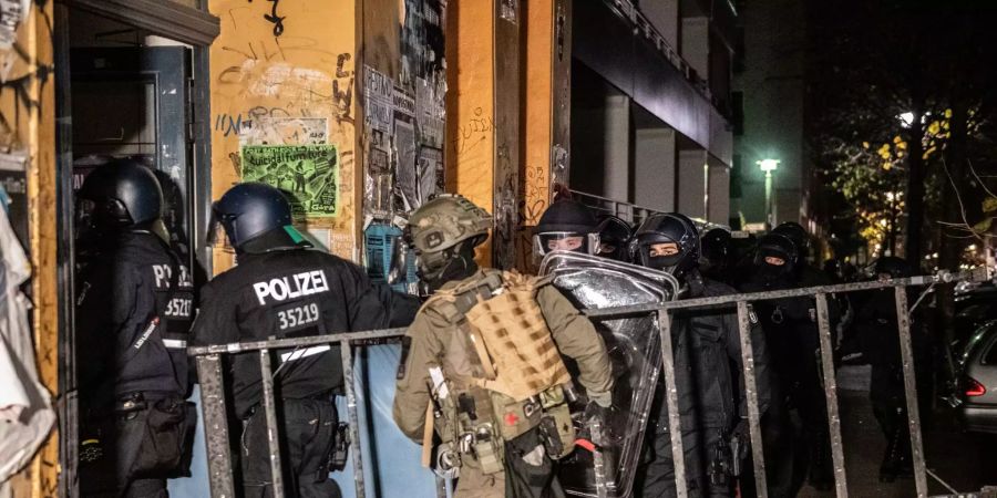 Polizeibeamte und ein SEk-Beamter gehen bei einer Razzia in ein Haus.
