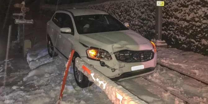 Ein Auto steht auf einem Bahngleis und es schneit.