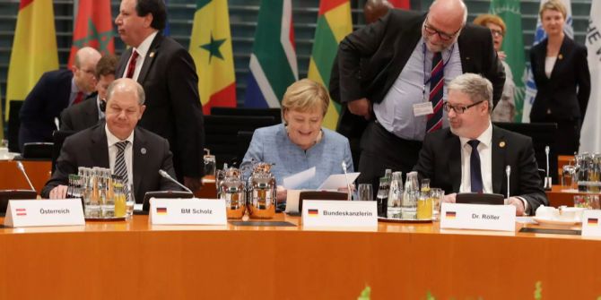 Dr. Lars-Hendrik Röller (r) sitzt an einem Gipfel neben Bundeskanzlerin Angela Merkel (M).