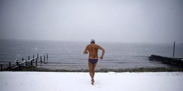 Ein Mann rennt an einem verschneiten Strand in Richtung Meer.