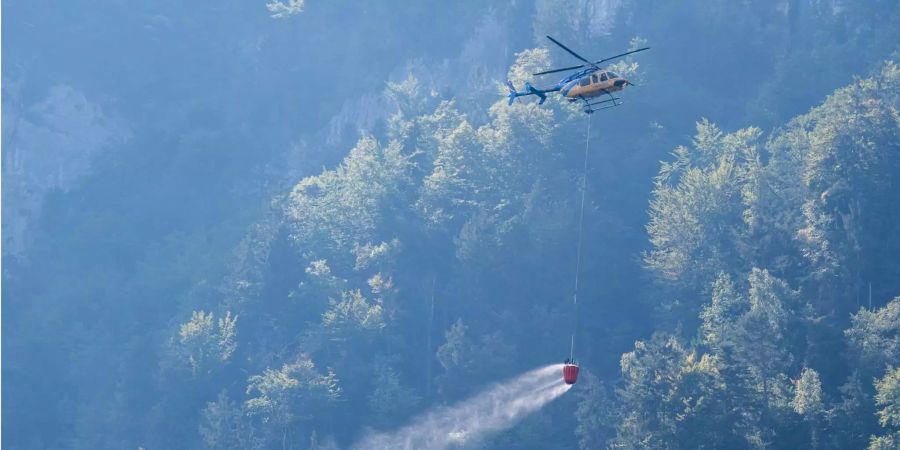 Ein Helikopter transportiert Löschwasser um den Brandherd nach einem Kleinflugzeugabsturz am Lopper zu löschen.